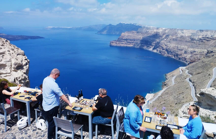 People seated at wine-tasting tables, captivated by the stunning island view. Savoring wine, soaking in beauty, creating unforgettable memories.